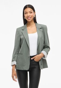 Groene blazer met een gestructureerd ontwerp, twee voorzakken en gestreepte manchetten. Draag je over een witte tanktop en zwarte broek. Gladde stofstructuur.