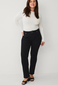Schwarze Jeans mit geradem Bein, ausgestattet mit Fronttaschen und einem Knopfverschluss, kombiniert mit einem enganliegenden weißen Langarmoberteil.