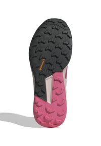 Suela de zapatilla de trail running en negro y rosa con tacos profundos para tracción. Presenta una superficie texturizada y un material de goma duradera.