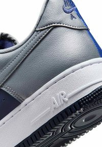 Zapatilla deportiva de cuero gris con detalles en azul marino, panel lateral texturizado, costuras visibles y suela de goma blanca con el logo "AIR".