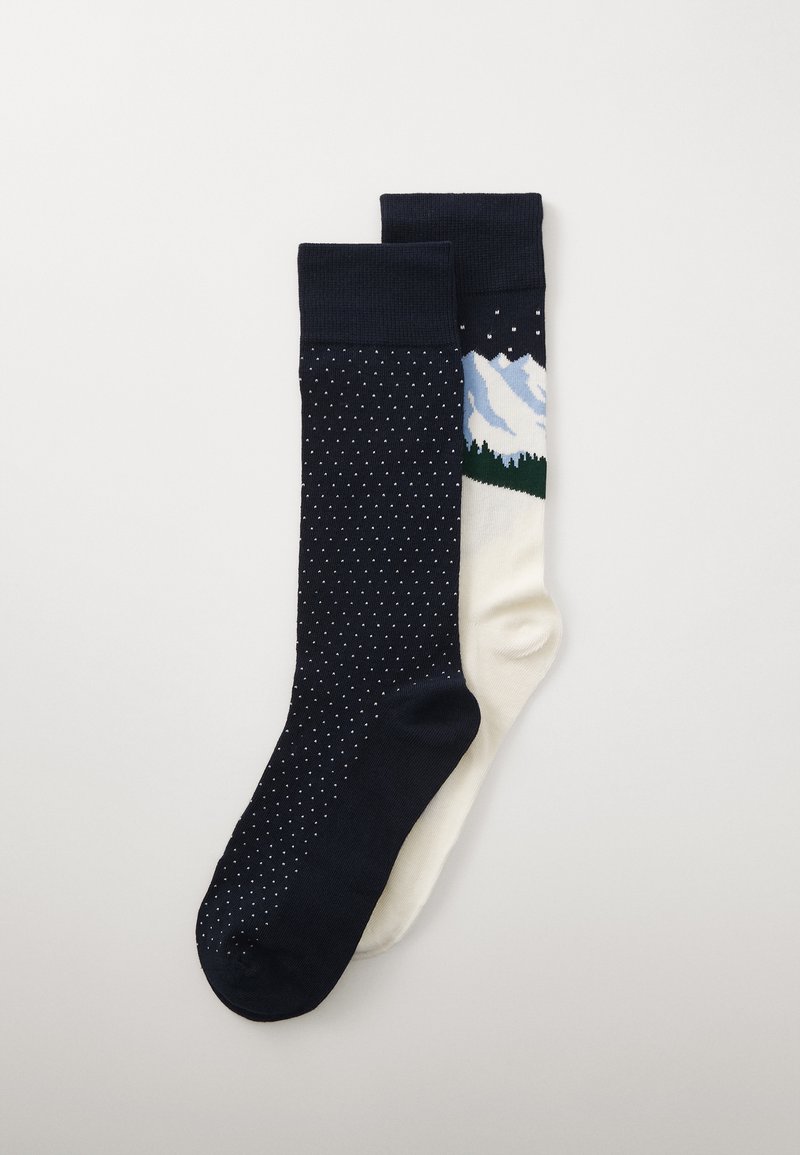 Meias com um lado azul-marinho com bolinhas brancas e um lado creme que retrata montanhas e árvores. Material de malha suave, comprimento até a metade da panturrilha.