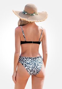 Czarny i biały bikini w wzory z regulowanymi ramiączkami, składające się z czarnej góry i majtek w stylu wysokiej talii. Szeroki kapelusz ze słomy z kwiatowymi akcentami.