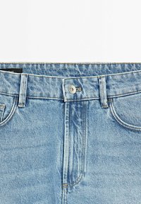 Světlé modré džíny z denimu s klasickým pětikapsovým designem, stříbrným zapínáním na knoflík a kontrastním šitím podél švů.