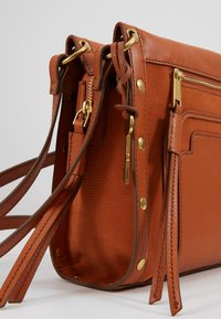 Brun læder crossbody taske med guldfarvet hardware, udstyret med en lynlåslomme, sidelister og justerbare stropper for personlig tilpasning af længden.