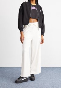 Chaqueta bomber negra recortada con puños acanalados, combinada con pantalones plisados blancos de pierna ancha. Zapatillas negras con plataforma y detalles en blanco.