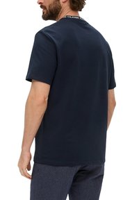 Granatowa bawełniana koszulka z krótkim rękawem, okrągłym dekoltem i charakterystyczną metką marki z tyłu kołnierza. Subtelna tekstura.