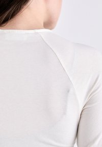 Helle beige Langarmbluse mit glatter Textur, Raglanärmeln und Rundhalsausschnitt, von hinten betrachtet.