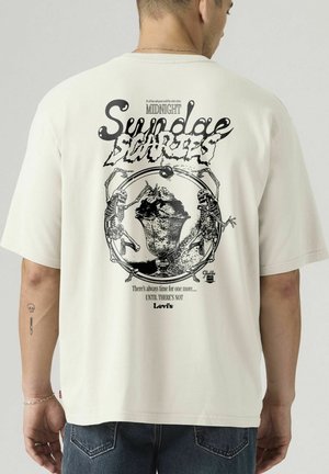 Mann trägt ein weißes T-Shirt mit schwarzem Motiv zweier Skeletten, die um ein Eisbecher tanzen, und Text mit der Anspielung "Midnight Sundae Disorders".