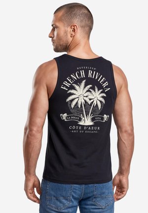 Mann mit kurzen Haaren, der ein schwarzes ärmelloses Shirt mit Palmenbaum-Design und dem Text "French Riviera" auf dem Rücken trägt, kombiniert mit blauen Jeans.