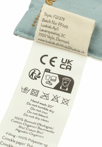 Šviesiai mėlynas audinio etiketė su priežiūros instrukcijomis, medžiagos detalėmis ir logotipu. Įtraukta juodų ikonų informacija apie plovimą, džiovinimą ir perdirbimą.