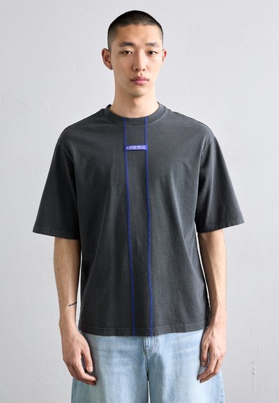 T-shirt da uomo grigio in cotone con maniche corte, caratterizzato da un patch logo blu e cuciture blu a contrasto davanti. Vestibilità casual.
