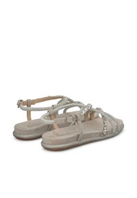 Beige Wildleder-Sandalen mit Strass-Akzenten, flacher Sohle, verstellbarem Knöchelriemen und Kreuzriemen-Design. Strukturiertes Finish an den Riemen.