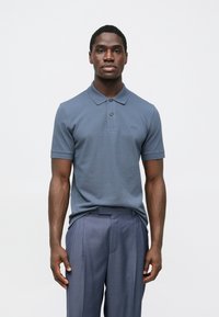 Zils polo krekls ar īsām piedurknēm, apkaklē ar apkakli un divu pogu plāksni, kopā ar gaisīgi pelēkām krokotām biksēm.