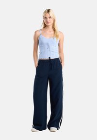 Light blue ribbed crop top with thin straps and a tie detail, paired with navy wide-leg pants featuring white side stripes.