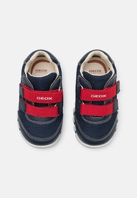 Sneaker blu navy con strap in velcro rossi, parte superiore in rete, suola in gomma e cuciture bianche. Presentano il marchio Geox sugli strap.