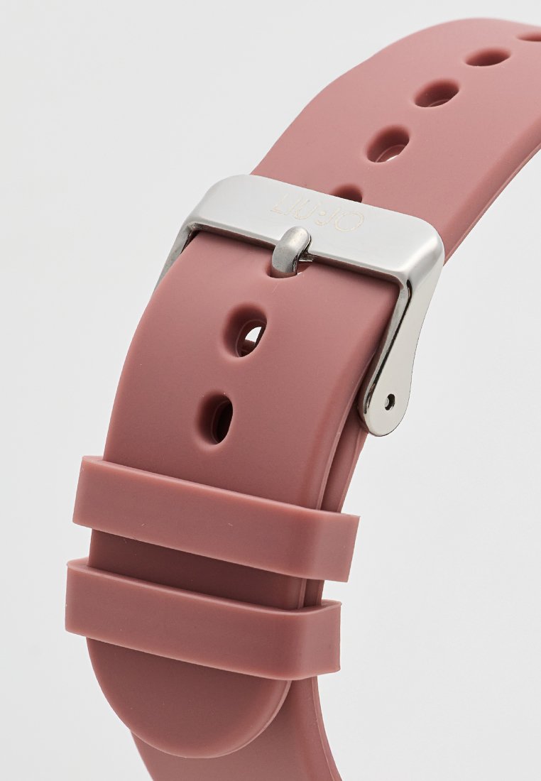 Bracelet de montre en silicone rose doux avec plusieurs trous d'ajustement, maintenu par une boucle en métal argenté et deux autres fixations en silicone.