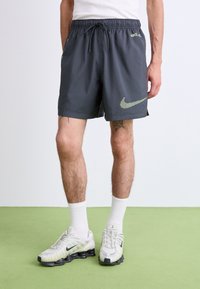 Mørkegrå Nike shorts med elastisk talje, sidelommer og et neongrønt logo sammensat af små prikker. Justeret pasform og letvægtigt materiale.