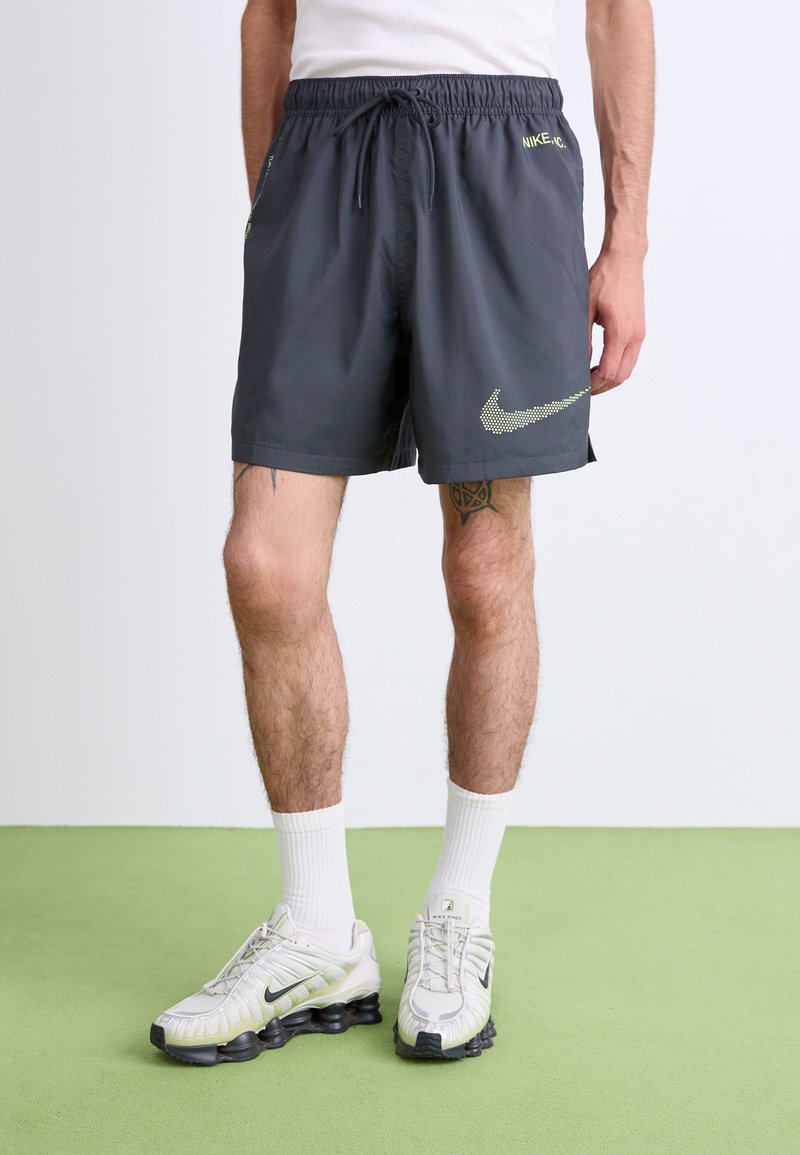 Mørkegrå Nike shorts med elastisk talje, sidelommer og et neongrønt logo sammensat af små prikker. Justeret pasform og letvægtigt materiale.