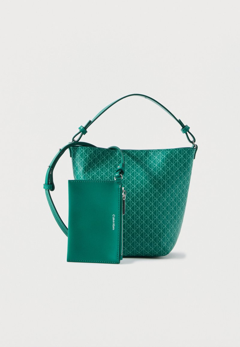 Πράσινη τσάντα χειρός με γεωμετρικό μοτίβο, ρυθμιζόμενο λουρί ώμου και συνδεδεμένη τσέπη με φερμουάρ που ταιριάζει, πάνω σε λευκό φόντο.