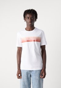 Bílý bavlněný tričko s horizontálním gradientním vzorem v růžové barvě a nápisem "Calvin Klein" vytištěným uprostřed. Krátké rukávy, kulatý výstřih.