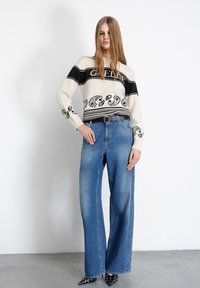 Maglioncino crema lavorato a maglia con righe nere e motivi decorativi, abbinato a jeans ampi a vita alta di colore blu chiaro e scarpe nere a punta.