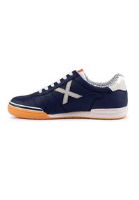 Zapatilla atlética azul marino con un logo X blanco, paneles texturizados y acentos naranjas. Presenta cordones blancos y una suela de goma.