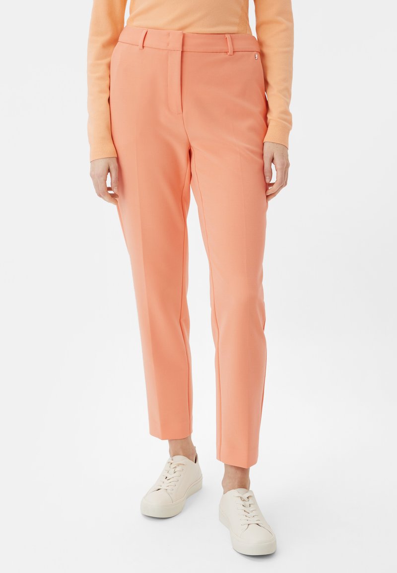 Peach-colored formal trousers with a tailored fit, creases down the front, belt loops, and paired with white sneakers.