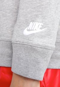 Grå Nike-tröja med vitt märke på vänster ärm, gjord av en mjuk bomullsblandning med ribbad mudd.