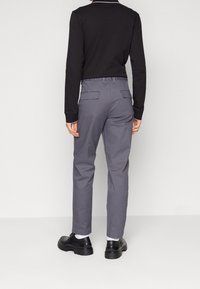 Gray pants with a tailored fit and elastic waistband, featuring back pockets. Worn with black shoes and a long-sleeve black top.