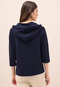 Felpa con cappuccio blu navy, caratterizzata da un design a coste testurizzate e maniche a tre quarti, con una vestibilità rilassata e una finitura semplice e pulita.