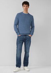 Blauer, strukturiert gestrickter Pullover mit rundem Ausschnitt, kombiniert mit hellblauen Jeans und weißen Sneakers. Einfaches und lässiges Outfit.