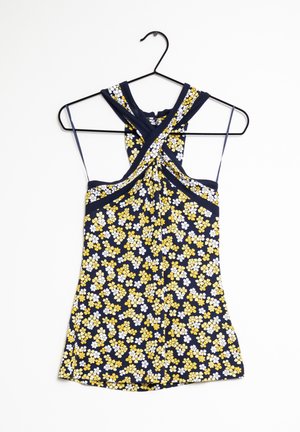 Top sans manches bleu marine à bretelles croisées et motif floral jaune et blanc, suspendu sur un cintre noir devant un fond blanc.