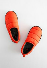 Fuzzy orange tofflor med en texturerad svart sula, som har ett mjukt grått inre och dragöglor för enkel påtagning.