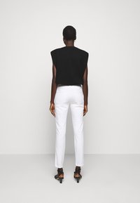 Top negro sin mangas con hombros acolchados, combinado con jeans blancos de pierna recta. Textura elegante, diseño minimalista y tacones negros con tiras.