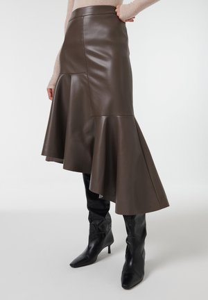 Jupe en cuir marron avec un ourlet évasé, texture lisse et taille haute. Associée à des bottes noires montantes.