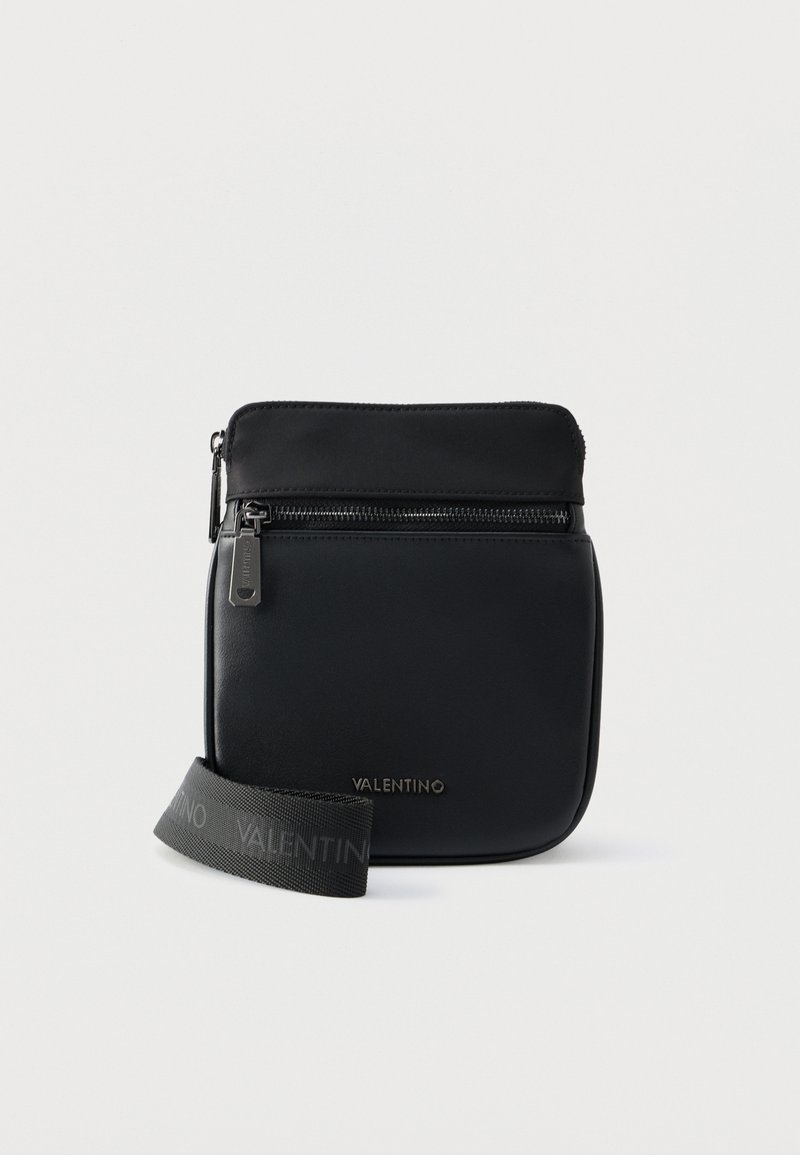 Μαύρη τσάντα Valentino χιαστί με μπροστινή τσέπη με φερμουάρ και ρυθμιζόμενο ιμάντα με λογότυπο σε λευκό φόντο.