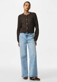 Cardigan marrón de canalé con cuello redondo y cierre de botones, combinado con jeans de pierna ancha en azul claro y zapatillas burdeos.