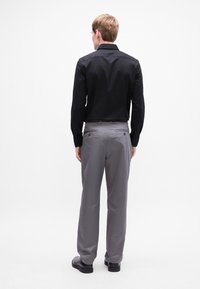 Zwarte overhemd met knopen, grijze broek, gladde stof, slim fit, met zakken en subtiele stiksels. Schoenen zijn zwart en gepolijst.