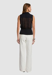 Blouse noire sans manches avec un dos transparent, taille ajustée et un design à col, associée à un large pantalon blanc. Texture de tissu lisse.