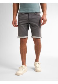 Shorts de mezclilla gris con dobladillos enrollados, con un diseño clásico de cinco bolsillos. Combinados con zapatillas de color blanco roto. Textura suave.