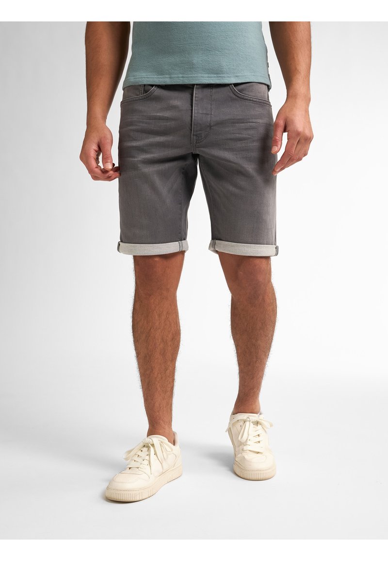 Shorts de mezclilla gris con dobladillos enrollados, con un diseño clásico de cinco bolsillos. Combinados con zapatillas de color blanco roto. Textura suave.