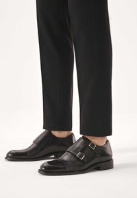 Schwarze Lederschuhe mit doppeltem Monkriemen, glänzendem Finish, abgerundeter Spitze und silbernen Schnallenakzenten, kombiniert mit maßgeschneiderten schwarzen Hosen.