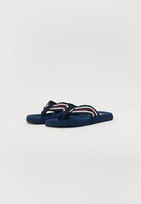 Tongs bleues avec des sangles en tissu marine ornées de rayures blanches et rouges, semelles en caoutchouc plates et une semelle intérieure texturée pour l'adhérence.