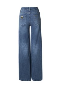 Plačių kojų mėlynos spalvos džinsai iš denimo su vidutinio aukščio liemeniu, dviem užpakalinėmis kišenėmis ir subtiliu išblukimu. Ant dešinės užpakalinės kišenės yra prekės ženklo etiketė.