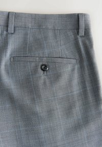 Pantalon de costume gris à carreaux avec une seule poche arrière fermée par un bouton noir et des passants de ceinture le long de la taille.