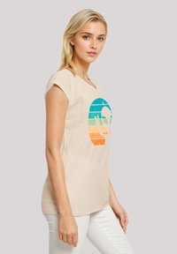 Light beige cotton t-shirt with a large graphic of a colorful alien head, featuring horizontal stripes in blue, green, orange, and yellow.