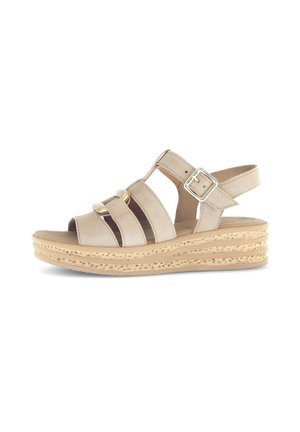 Beige sandal featuring multiple horizontal straps, a closed heel, and a buckle. The sole is tan with a textured, woven design.