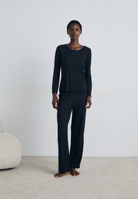 Mjukt, svart ribbat lounging-set med långa ärmar och fransade kanter. T-shirten har en rund halsringning; de matchande byxorna är vida.