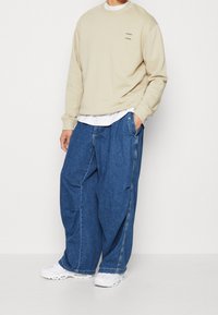 Beige mikina s výšivkou, kombinovaná s oversized modrými džínami. Bílé tenisky dotvářejí vzhled. Neformální styl a pohodlný střih.