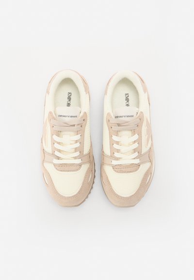 Zapatillas beige y crema con parte superior de malla y ante, puntera redondeada, cordones blancos y detalles de logo en la lengüeta y el lado.